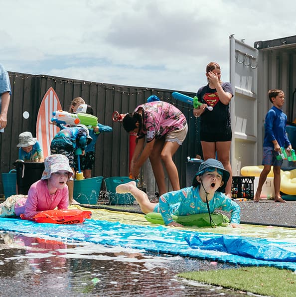 Kids playing on a water slip-and-slide at a City on a Hill Church family event